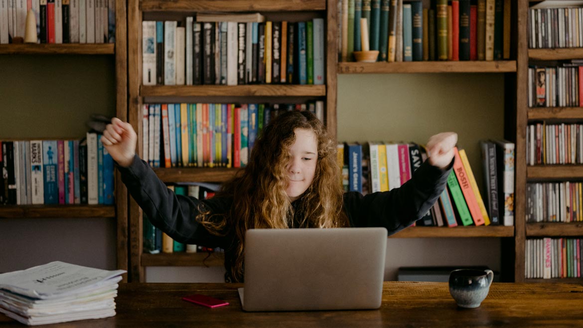 Student looking at laptop screen in front of bookshelves full of books