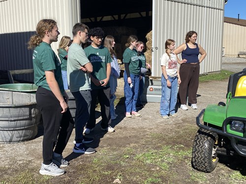 A group of Day of Service volunteers receiving direction from a community partner for cleaning a barn space at the Equine Center for Learning.