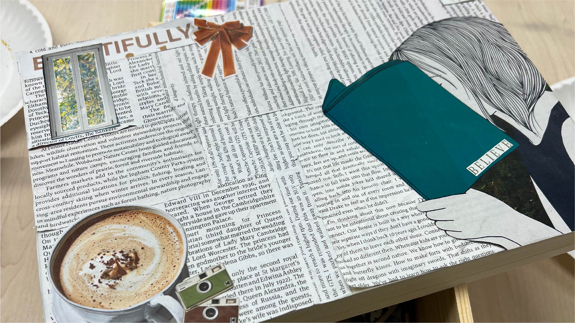 A completed collage on a wooden surface, covered with newspaper clippings and images. Prominent elements include a cup of coffee, a camera, a window, and an illustration of a person reading a teal book labeled “BELIEVE.”