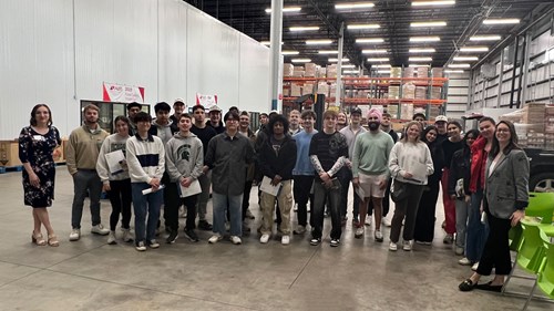Broad-SCM-GroupPhoto: A class photo of supply chain management capstone students with Greater Lansing Food Bank staff in the GLFB’s warehouse.