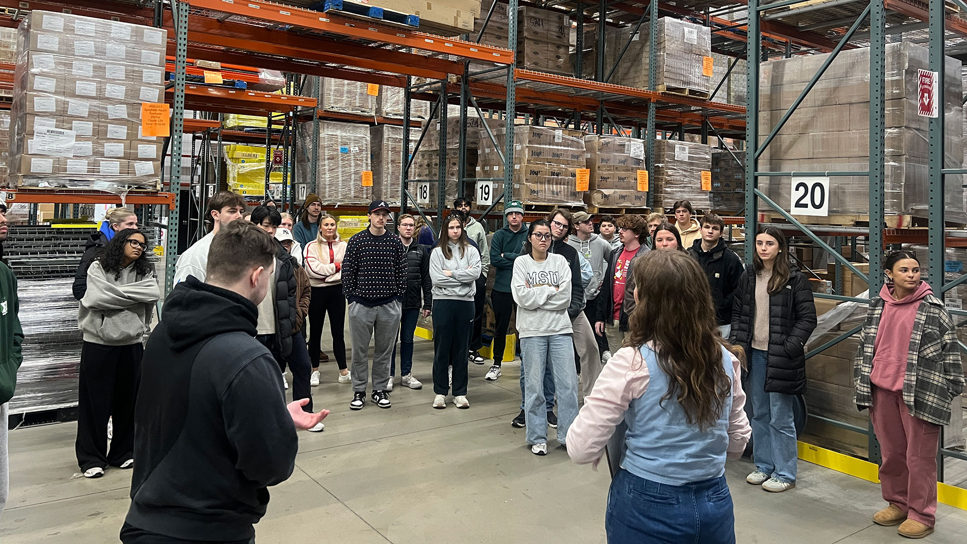 In a storage warehouse at the Greater Lansing Food Bank, GLFB staff and volunteers explain food bank distribution processes to supply chain management capstone students.