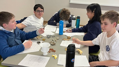 A group of young Michigan Junior Classical League students examines pottery fragments and replicas during a workshop.