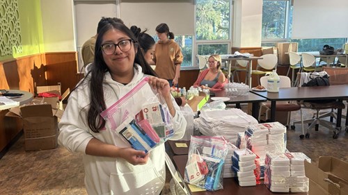 Scholar Jannet Garcia showing a bag of first aid and hygiene supplies that will be packed into a resource kit for an unhoused neighbor.