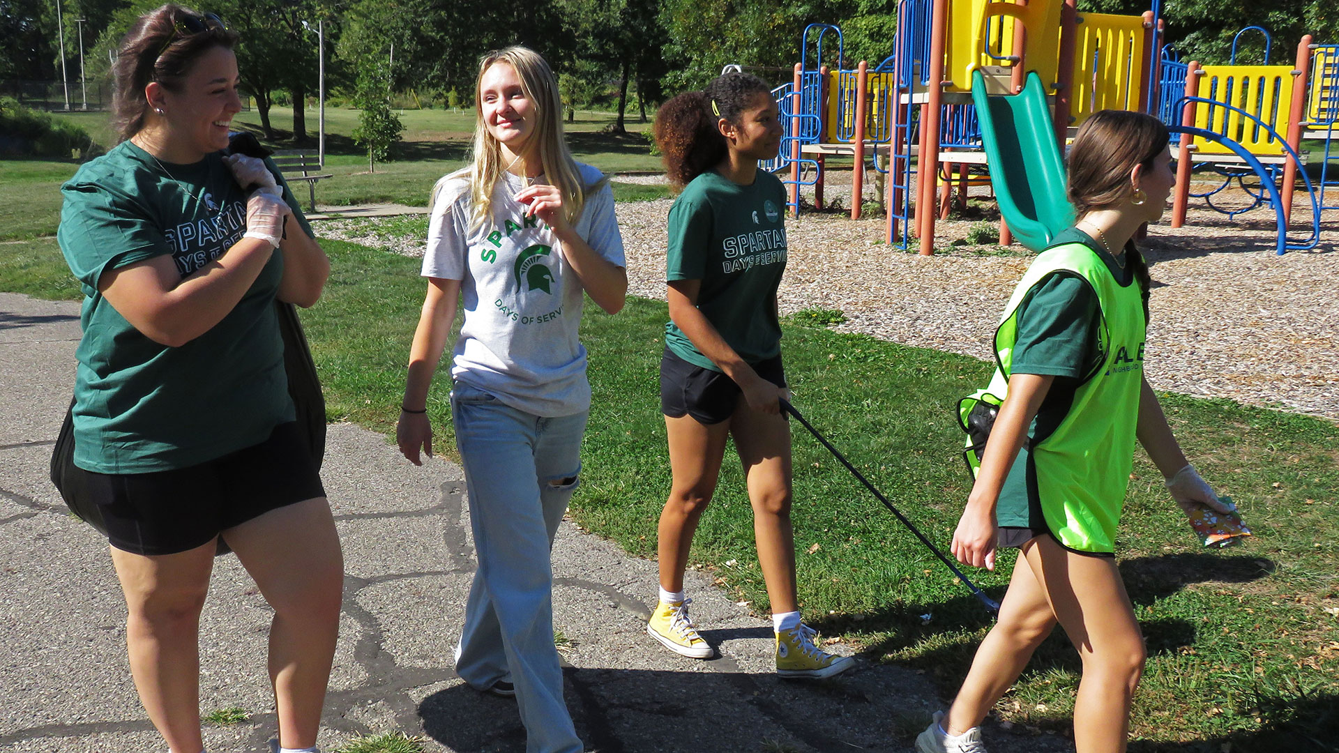 A group of Fall Day of Service volunteers with Allen Neighborhood Center walking and connecting as they return for lunch. Several have bags and grabbers for picking up trash, and one wears a bright yellow safety vest for distributing flyers in the neighborhood
