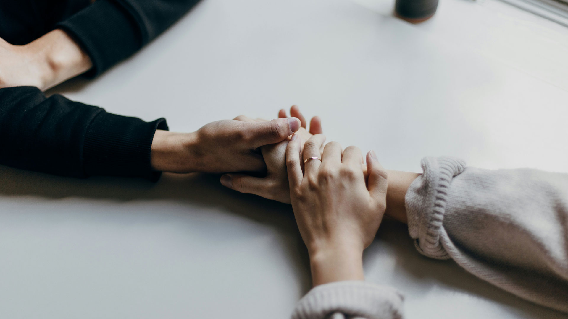 High-angle shot of two people gently holding hands across a neutral-toned table