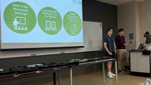 MSU VITA vice president Caiden Kippnick (left) and president Erich Schroeder (right) present a slide about milestones for the 2025-2026 academic year at MSU VITA’s end-of-year celebration meeting. Highlights on the slide include holding 14 tax bootcamp trainings, launching a client booking form on their website, and preparing international tax returns for the first time.